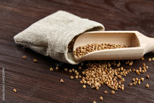 Buckwheat groats (hulled seeds) in burlap bag, scoop on wooden background