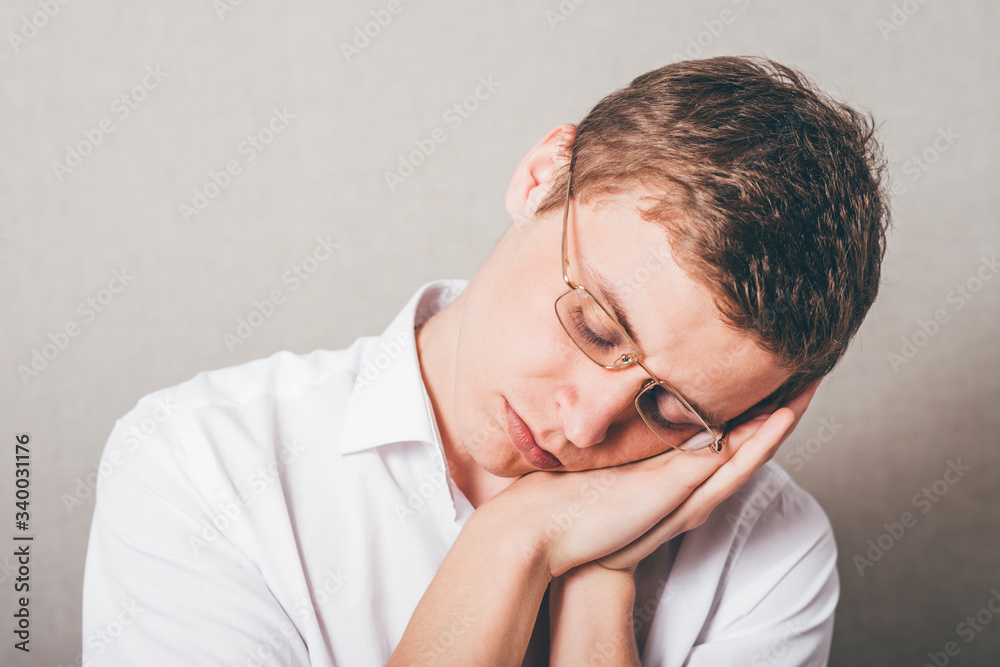 The man in glasses tired sleep. On a gray background. The man in glasses tired sleep. On a gray background.