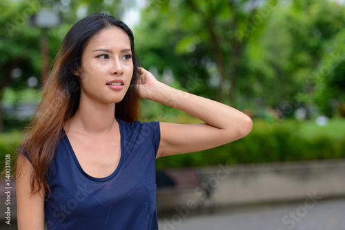 Young beautiful Asian businesswoman thinking in the park