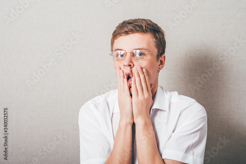 The man in glasses upset sad, hands on his cheeks. On a gray background.
