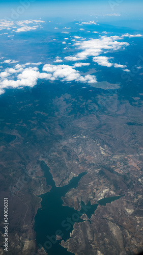 Aerial view of lake and mountains. View from a plane window. Beautiful landscape under the clouds and blue sky