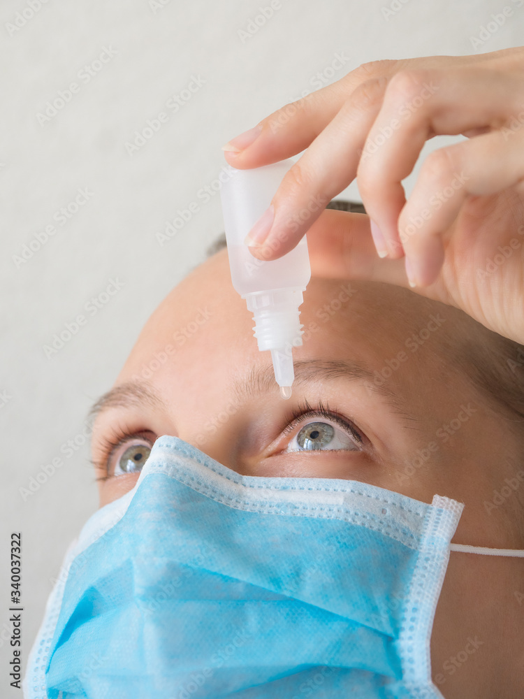 Woman in a medical mask using eye drops. Prevention of viral infections