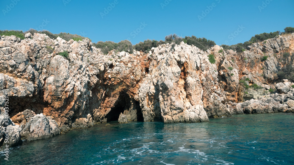 Beautiful deep sea with small waves and steep cliffs on the shores of the Mediterranean Sea with trees and caves.