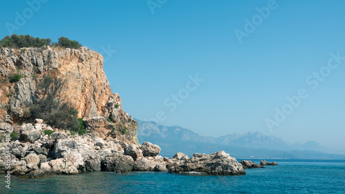 Beautiful deep sea with small waves and steep cliffs on shores of Sea with trees and caves against mountains in distance