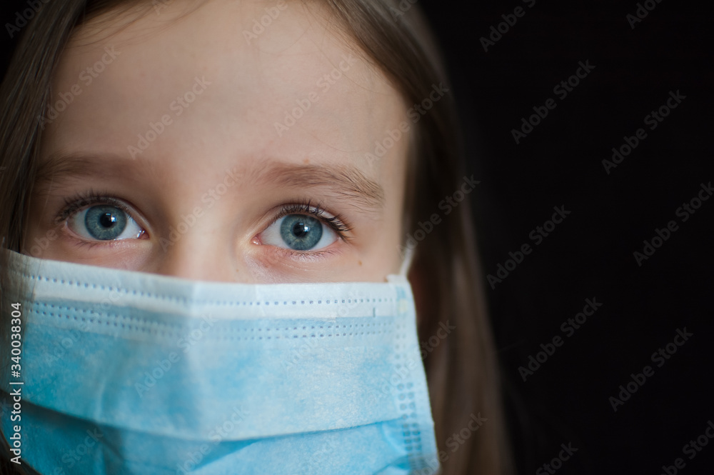 Close-up portrait of little defenseless girl on black backgound in blue disposable mask for protection of Coronavirus Covid-19 during self-isolation at home Close-up portrait of little defenseless girl on black backgound in blue disposable mask for protection of Coronavirus Covid-19 during self-isolation at home