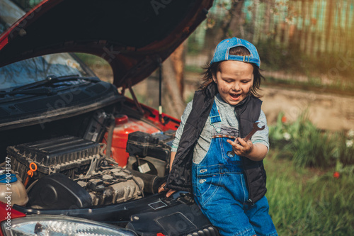 Little child trying to fix broken real car. Dreaming to be at auto technicial