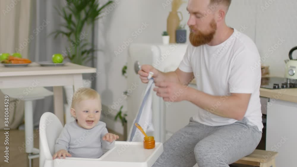 Medium shot of caring father with beard wiping mouth of adorable toddler girl after feeding her Medium shot of caring father with beard wiping mouth of adorable toddler girl after feeding her