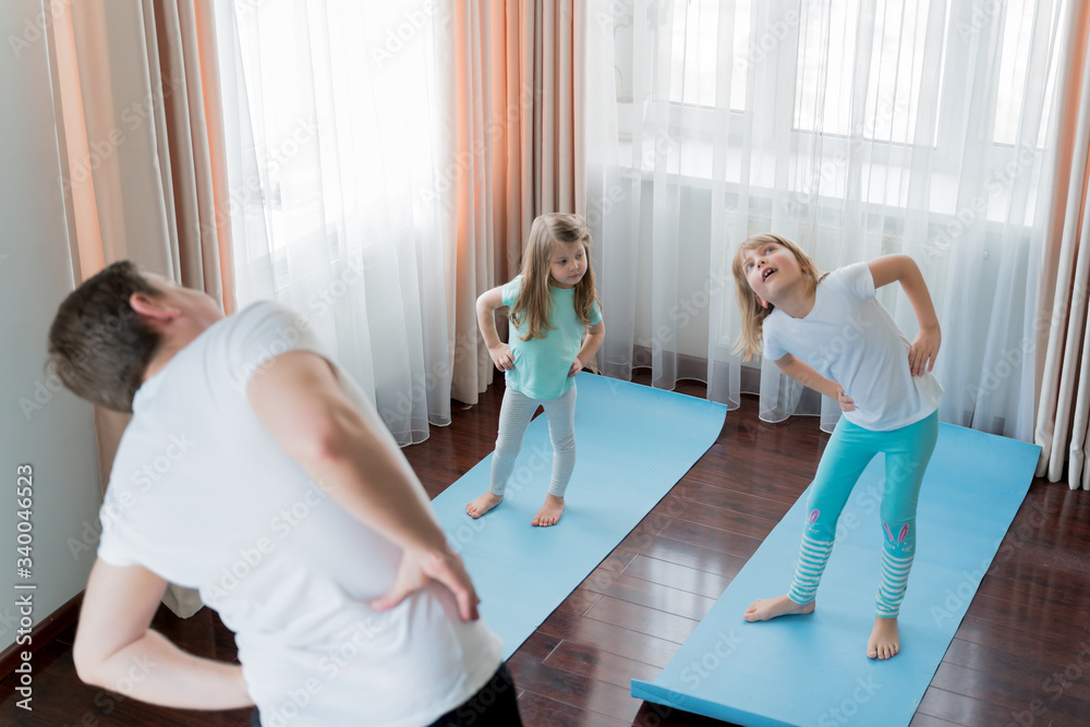 Obraz premium Home workout in flat.Dad teaching little girls fitness, daughters. Physical morning exercises on blue yoga mats.Family children fun.Healthy indoor activity.Quarantine,coronavirus covid-19.No equipment