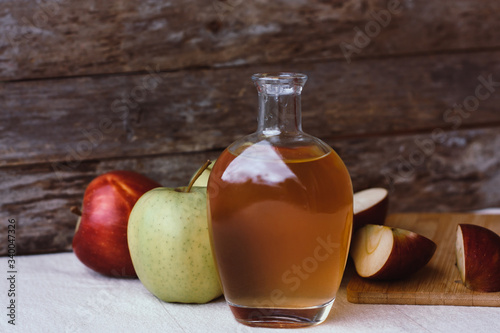 Apple organic vinegar in glass pitcher with ripe fresh red and yellow apples on wooden background. Healthy organic food concept