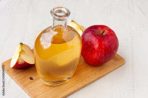 Apple organic vinegar in glass pitcher with ripe fresh red and yellow apples on wooden cutting board. Healthy organic food concept