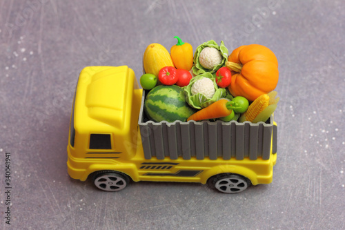 Fototapeta Naklejka Na Ścianę i Meble -  agricultural products transportation. A yellow toy truck delivering  fresh fruits and vegetables  in a container.