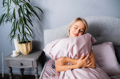 Beautiful blonde hugs a pillow in bed with her eyes closed. Woman with a pillow. Pillow for sleeping.