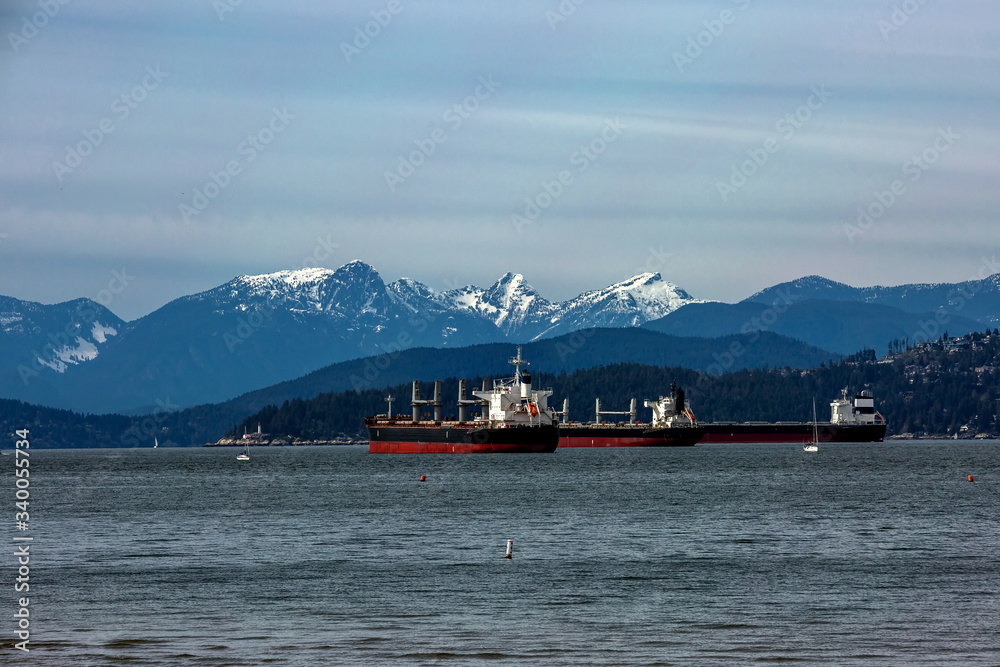 Ocean Tankers in Vancouver Harbor шт a sunny  day against the backdrop of a snow covered  mountain ridge  and cloudy sky