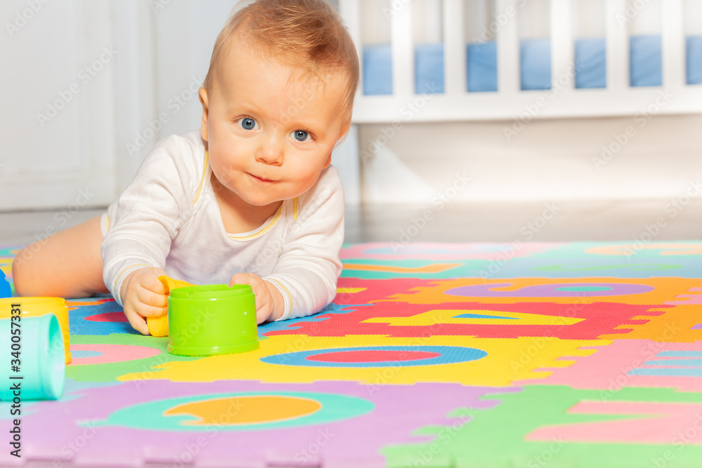 Beautiful baby toddler crawl on the floor of nursery grabbing toys near crib looking at camera Beautiful baby toddler crawl on the floor of nursery grabbing toys near crib looking at camera