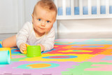 Beautiful baby toddler crawl on the floor of nursery grabbing toys near crib looking at camera
