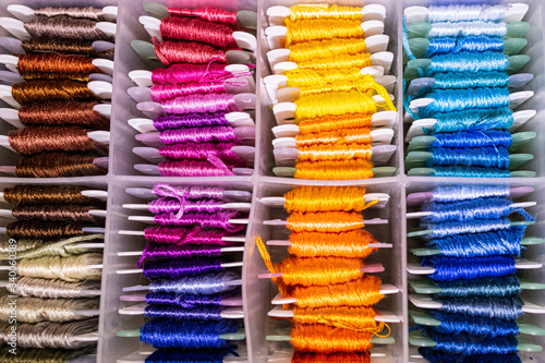Mouline threads arranged by color for hand embroidery and needle in a transparent plastic box. Top view. 
