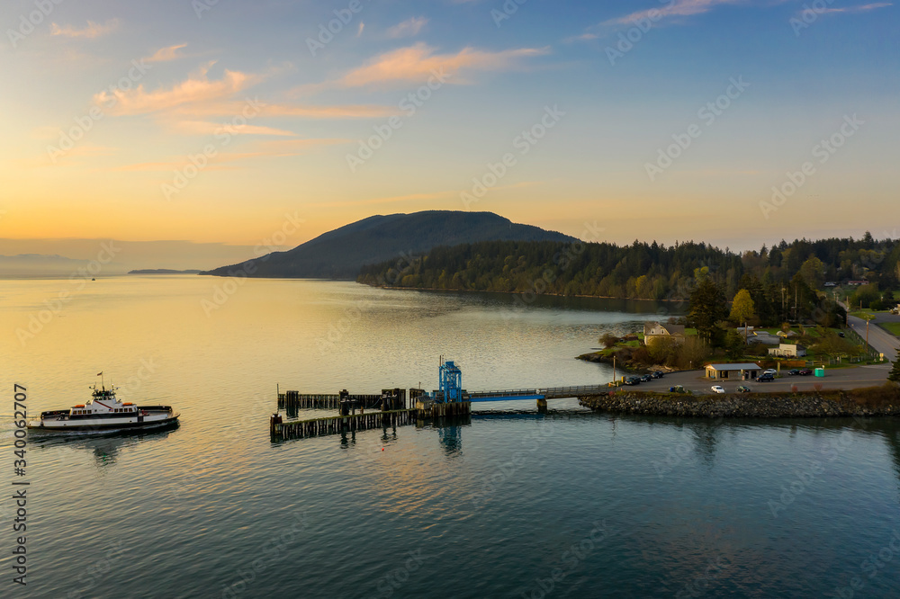 Aerial View of a Ferry Boat Landing at the Island Dock. Aerial shot of a small 21 car ferry landing at the Lummi Island ferry dock on a beautiful sunlit morning in the the Pacific Northwest, USA. Aerial View of a Ferry Boat Landing at the Island Dock. Aerial shot of a small 21 car ferry landing at the Lummi Island ferry dock on a beautiful sunlit morning in the the Pacific Northwest, USA.