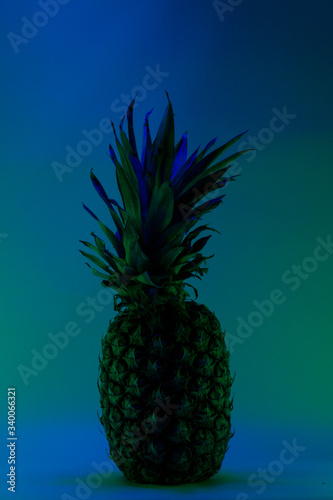 Whole shot of pineapple illuminated with orange led lights in the background and cyan fruit