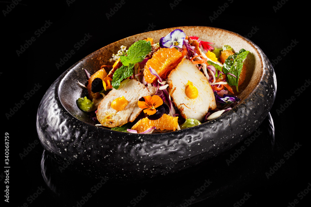 Asian salad dish with sliced chicken mint leaves orange fresh pulps and flower decoration in black bowl. Appetizer photo in plain background best use for fine dine in restaurant menu. Asian salad dish with sliced chicken mint leaves orange fresh pulps and flower decoration in black bowl. Appetizer photo in plain background best use for fine dine in restaurant menu.