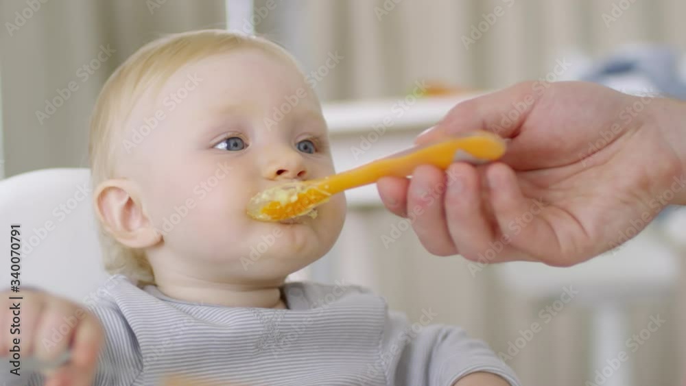 Close up of hands of unrecognizable father feeding puree to adorable baby girl with blond hair Close up of hands of unrecognizable father feeding puree to adorable baby girl with blond hair
