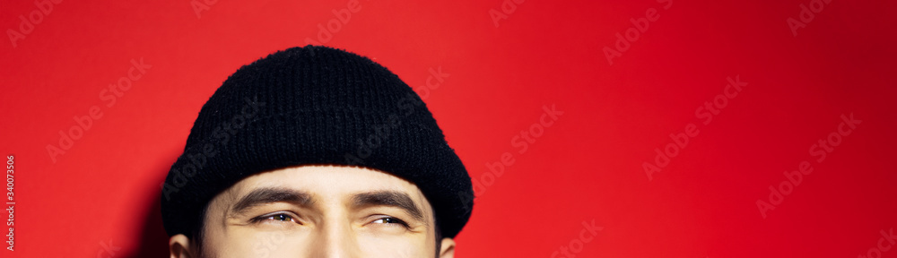 Close-up of smiling eyes of asian guy wearing black beanie hat, panoramic portrait on red background. Close-up of smiling eyes of asian guy wearing black beanie hat, panoramic portrait on red background.