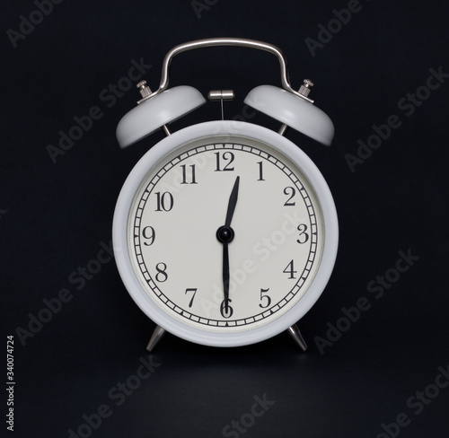 Old-style alarm clock, black and white, it's half past twelve.