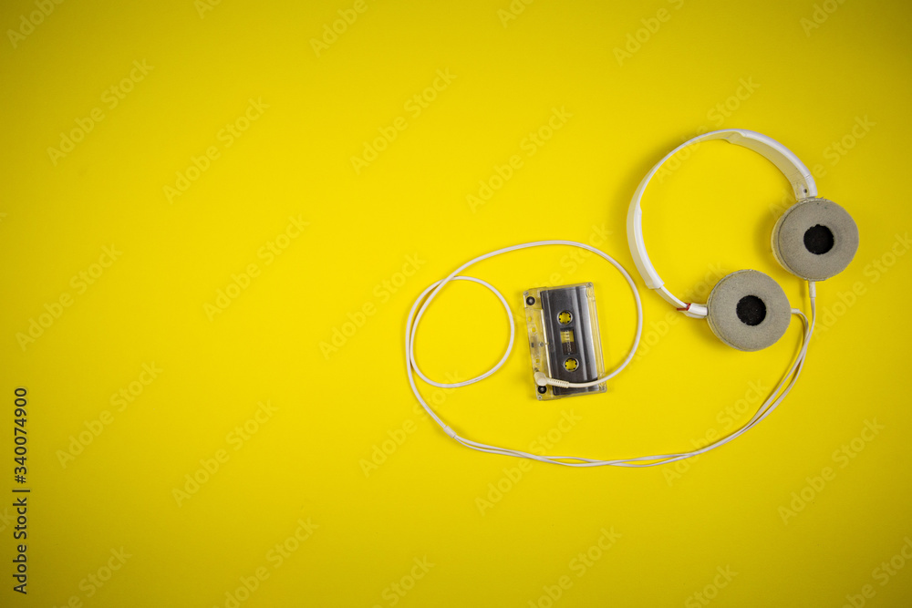 Audio cassette tape and modern headphones on a yellow background