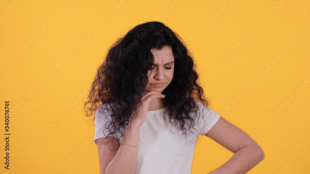 Portrait of beautiful young woman with black curly hair is sad and annoyed isolated on yellow background shot in 4k Portrait of beautiful young woman with black curly hair is sad and annoyed isolated on yellow background shot in 4k