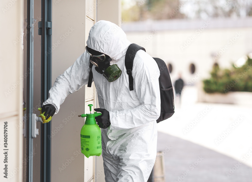 Quarantine, coronavirus infection. A man in protective equipment disinfects with a sprayer in the city. Cleaning and Disinfection at the street. Protective suit and mask. Epidemic.