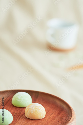 Three bright colorful mochis on a wooden plate and a coffee cup on a beige fabric.