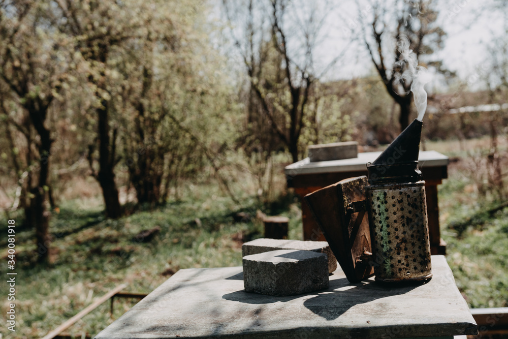 Chimney for flashing bees. Chimney stands near beehives.The beekeeper's tool. Bee smoker smoking. Chimney for flashing bees. Chimney stands near beehives.The beekeeper's tool. Bee smoker smoking.