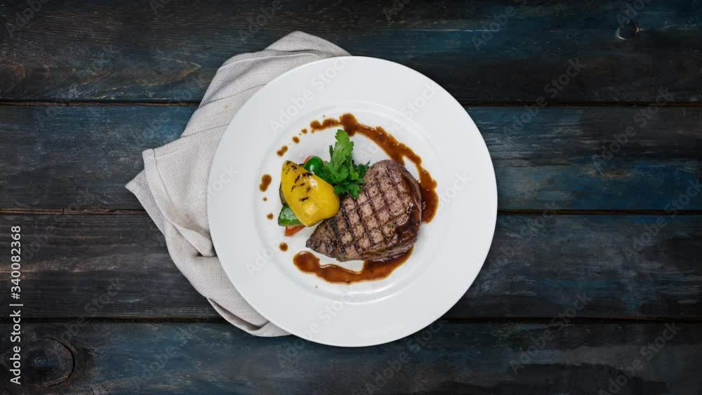 Veal steak with grilled vegetables rotates on a plate. Top view. Veal steak with grilled vegetables rotates on a plate. Top view.