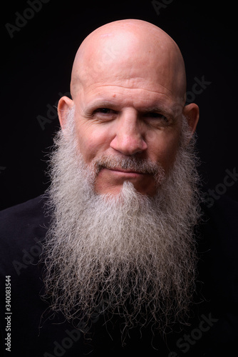 Mature bald bearded man against black background