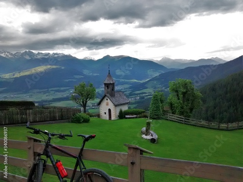 Fotografija Bicycle And Chapel On Field Against Mountains