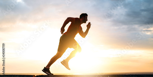 Fototapeta Naklejka Na Ścianę i Meble -  Attractive male runner in motion at sunset. Sport lifestyle. A man with athletic body in sportswear and sneakers runs at sunset