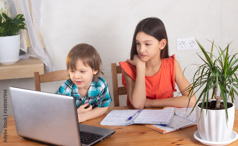 Elder sister with little brother watching video on laptop at home. Girl with unhappy face, boy bothering her. Home quarantine and self-isolation, siblings relations concept Elder sister with little brother watching video on laptop at home. Girl with unhappy face, boy bothering her. Home quarantine and self-isolation, siblings relations concept