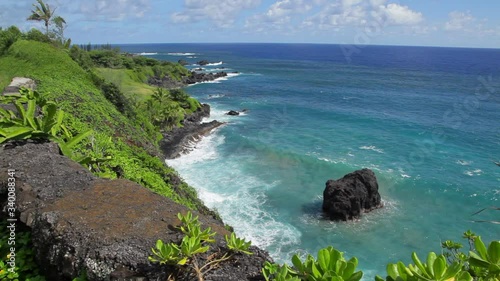 Rugged lava shoreline past Hana on the way to Kipahulu on Maui seen from a steep cliff,  showing deep blue ocean with white waves crashing to the lava rock shore below on a sunny Hawaii day, photo