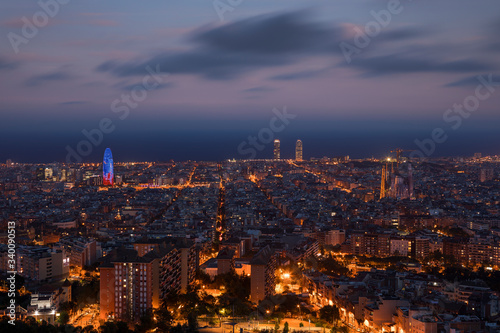 Illuminated skyline with cathedral Sagrada Familia and tower Torre Agbar in Barcelona during night, street lights from Bunkers del Carmel.