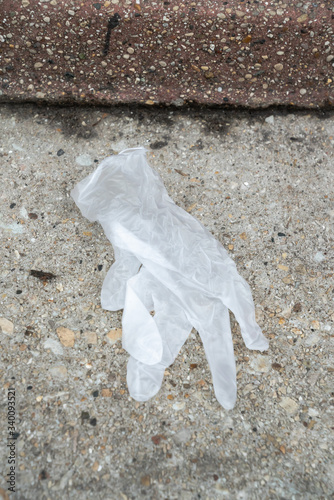 Used white plastic, rubber or latex medical glove lays discarded on the sidewalk in Chicago littering the street in garbage used for protection from the COVID-19 or coronavirus outbreak and pandemic.