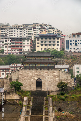 Baidicheng, China - May 7, 2010: Qutang Gorge on Yangtze River. Portrait of historic town Gate and highrise housing under White mist over hills. Long steep stairway leads up.