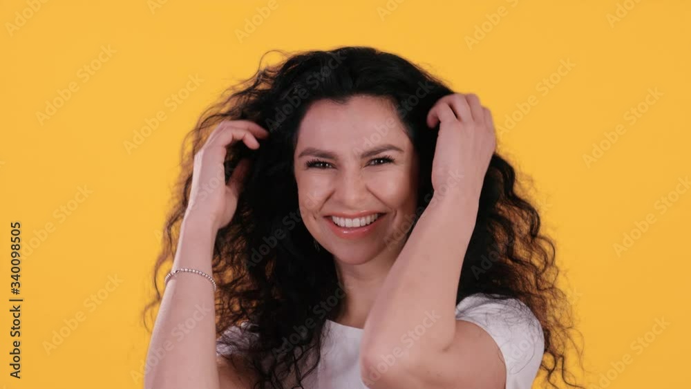 Portrait of beautiful young woman with black curly hair is laughing and shaking her head isolated on yellow background shot in 4k Portrait of beautiful young woman with black curly hair is laughing and shaking her head isolated on yellow background shot in 4k