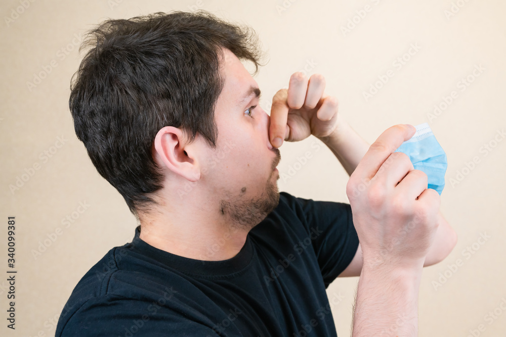 Naklejka premium A young guy puts on a medical mask. Hands clamped over his nose. It is important to wear a mask during the risk of infection. Medical concept.