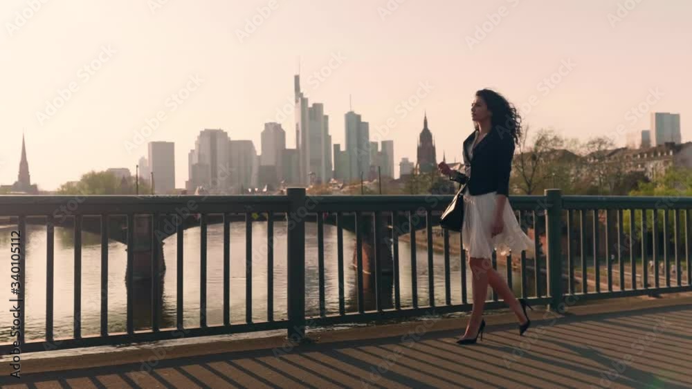 Beautiful business woman with black hair walking on bridge with skyline frankfurt and river main in background shot in 4k Beautiful business woman with black hair walking on bridge with skyline frankfurt and river main in background shot in 4k