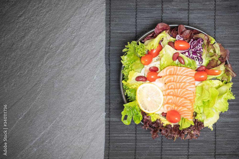 Salmon salad with various kinds of vegetables is a high-quality health care food and delicious. has low calorie and high vitamin content. Place in black bowl on the black stone table. with copy space