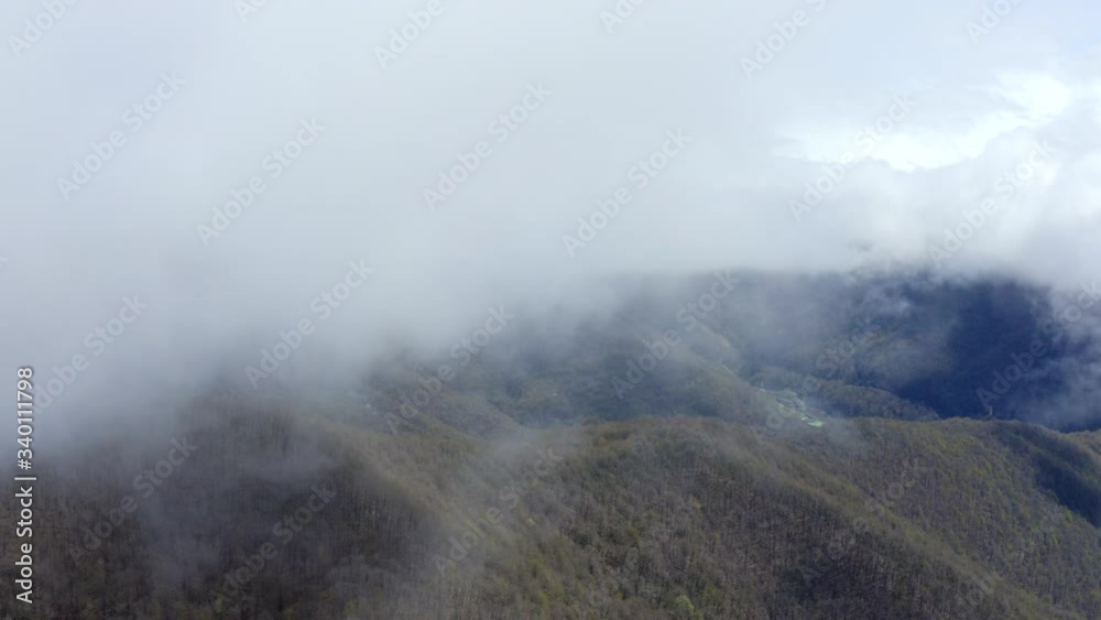 Clouds over mountain valley view from flying drone. Misty haze covering highlands aerial view. Spring mountain expanses in foggy haze from bird above Clouds over mountain valley view from flying drone. Misty haze covering highlands aerial view. Spring mountain expanses in foggy haze from bird above