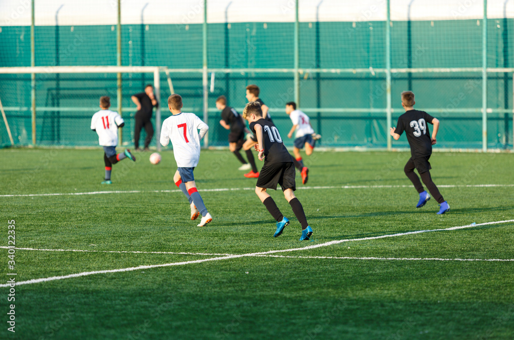 Obraz premium Boys in white black sportswear running on soccer field. Young footballers dribble and kick football ball in game. Training, active lifestyle, sport, children activity concept