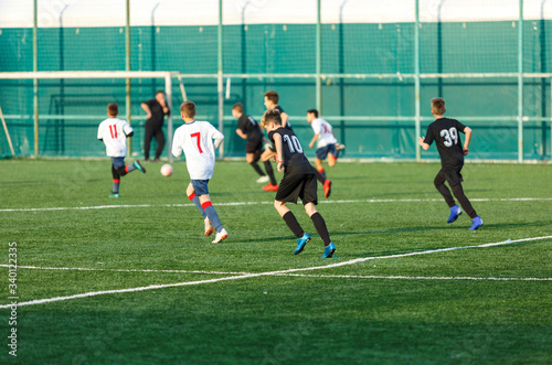 Boys in white black sportswear running on soccer field. Young footballers dribble and kick football ball in game. Training, active lifestyle, sport, children activity concept