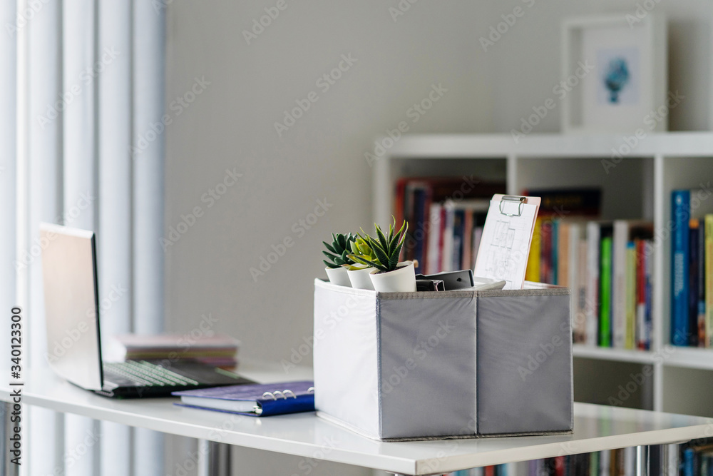 Box with personal items stuff packed on the white table in the office or home in day by the laptop ready to move after being fired or got the job at work place side view Box with personal items stuff packed on the white table in the office or home in day by the laptop ready to move after being fired or got the job at work place side view