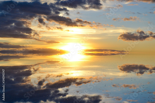 Sunrise or sunset in Uyuni salt flat (Bolivia) the biggest salar in the world covered with water and reflecting like a mirror the sky, the clouds and the sun in an orange, blue, white and yellow image © Alejandro