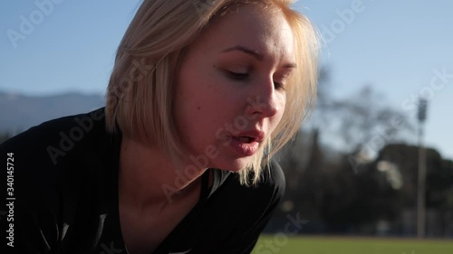 Girl athlete straightens her hair before a run in an open stadium on a clear summer day. Inhales and exhales deeply. And makes a breakthrough at the start.